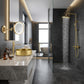 Modern bathroom interior with a large gold-framed mirror, round gold vessel sink on a marble countertop, and a walk-in shower with a rain head and gold shower hardware against dark gray stone walls.